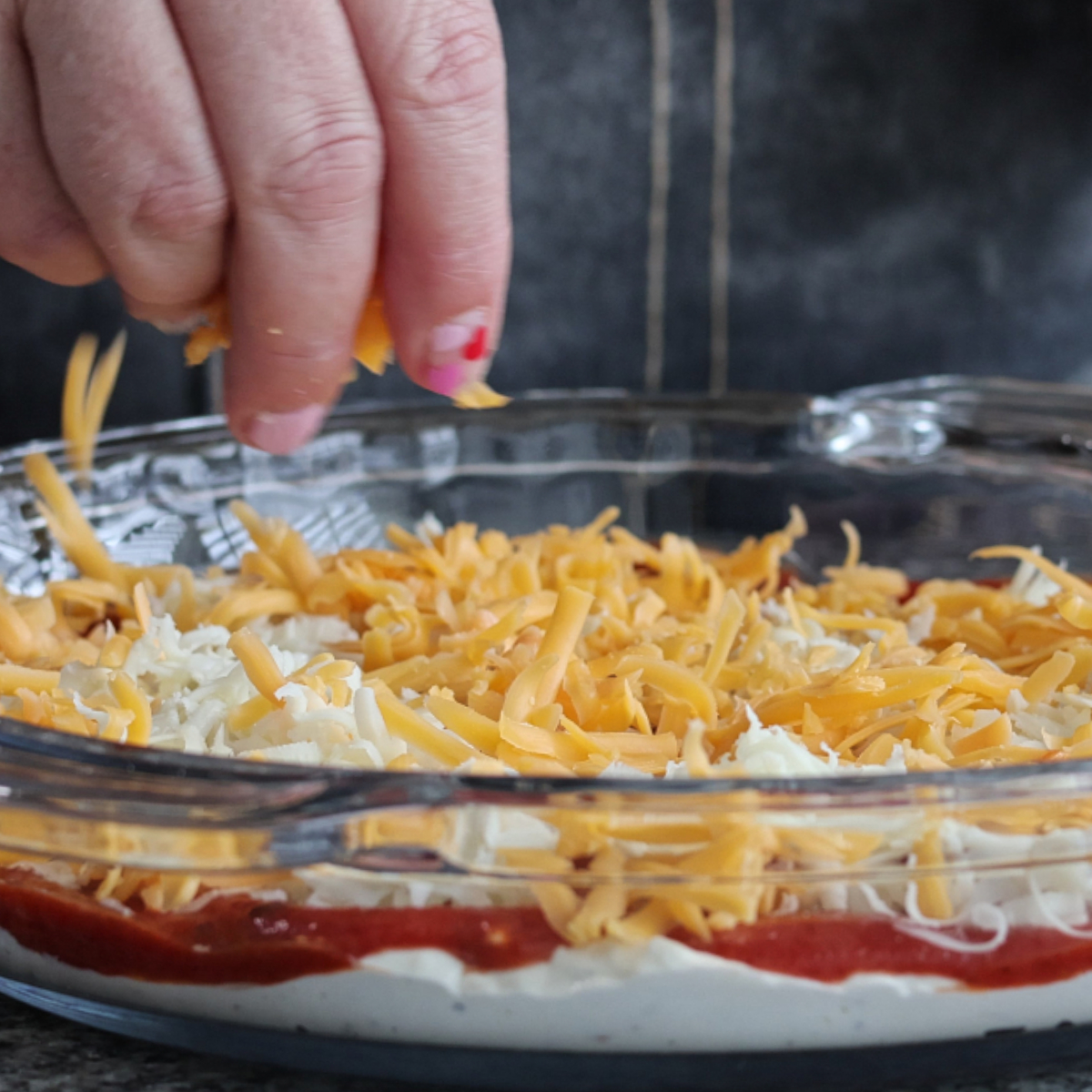 sprinkling cheddar and mozzarella cheeses over top of pizza dip.