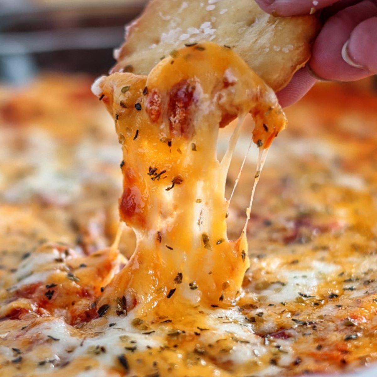 pizza dip with cheese pull on a homemade ritz cracker.