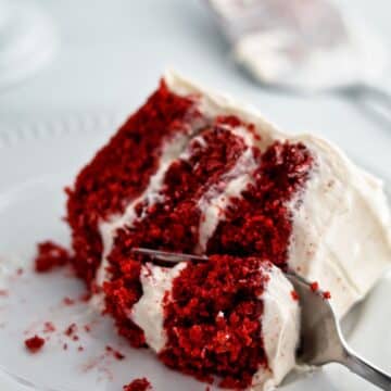 slice of gf red velvet cake on white plate with fork cutting through it.