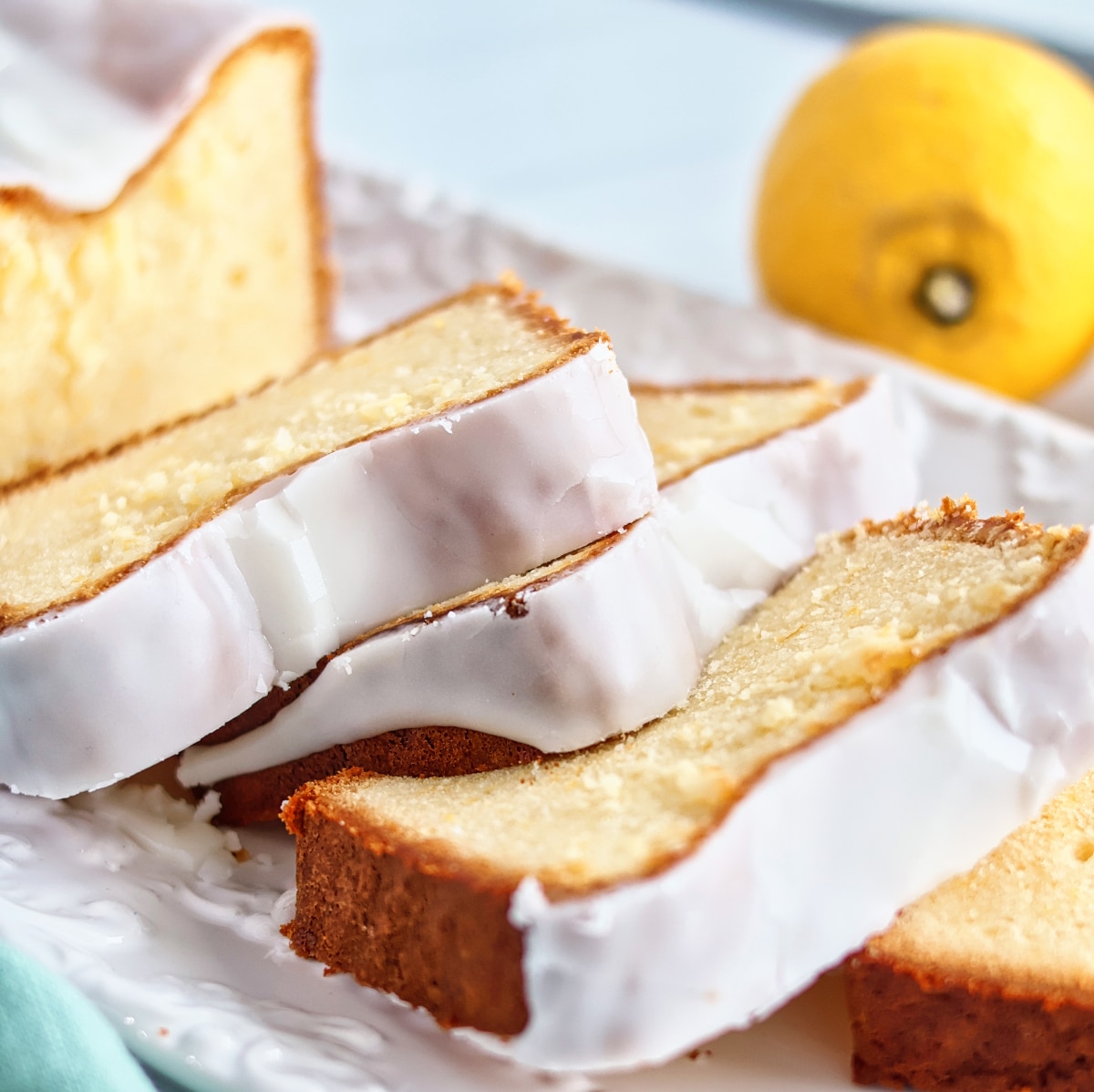 slices of gluten free lemon loaf cake on white rectangular platter with whole lemons in the background.