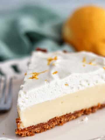 gluten free lemon pie on white scalloped plate with lemon and light green towel in the background.