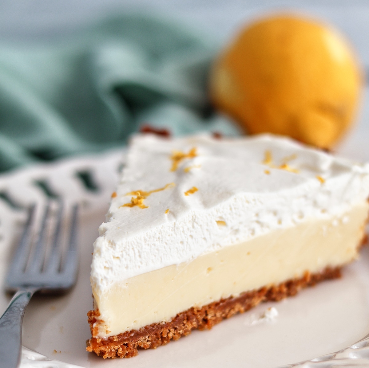 gluten free lemon pie on white scalloped plate with lemon and light green towel in the background.