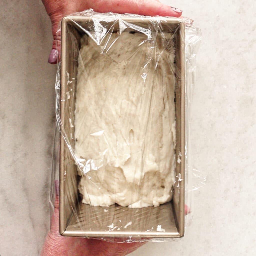 covering dough in gold loaf pan with plastic wrap.