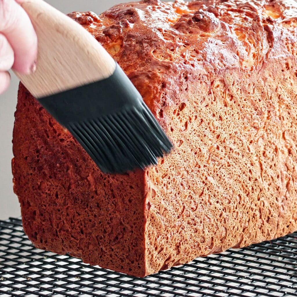 brushing melted butter on freshly baked bread loaf on wire rack.