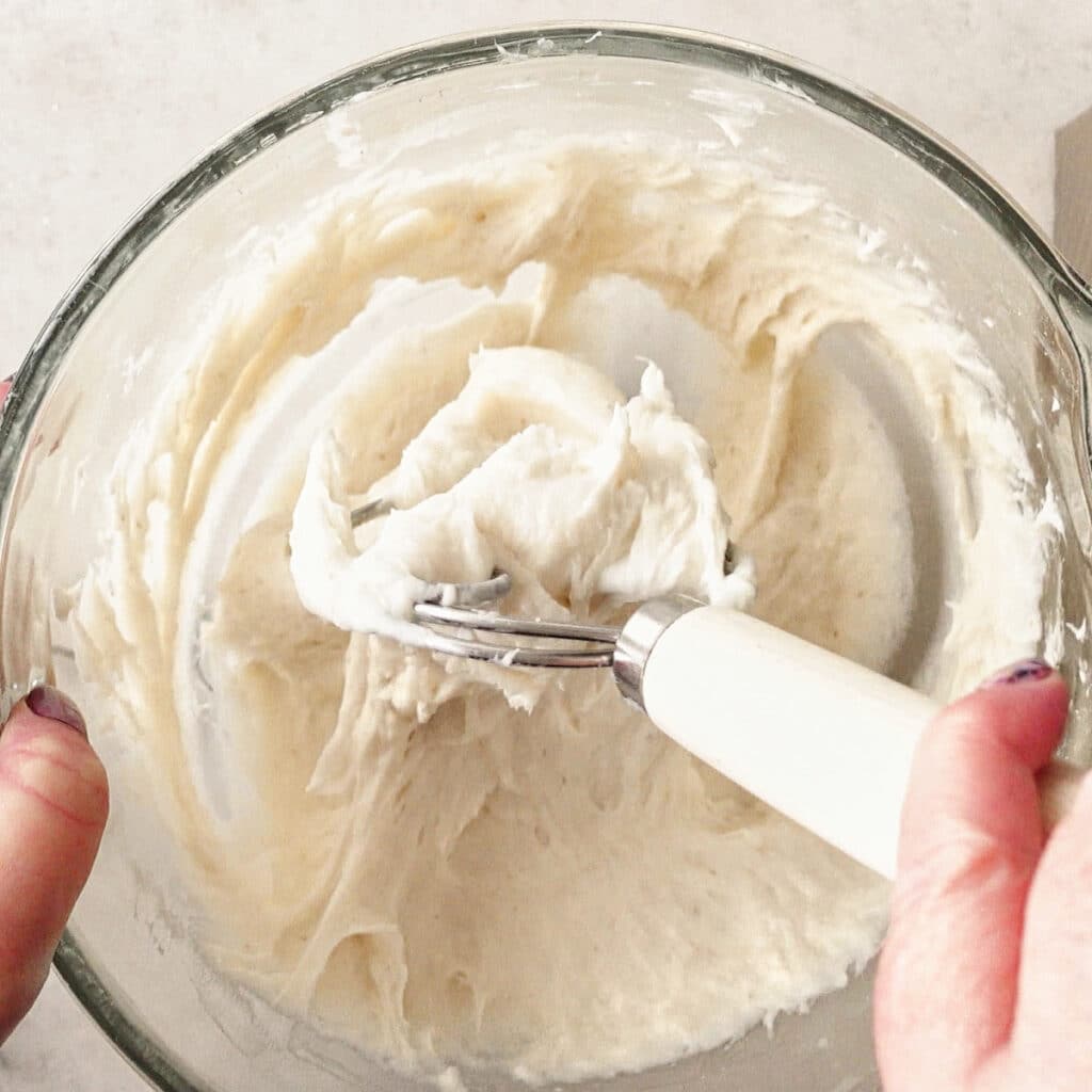 using a Danish dough whisk to deflate the dough in the glass bowl.