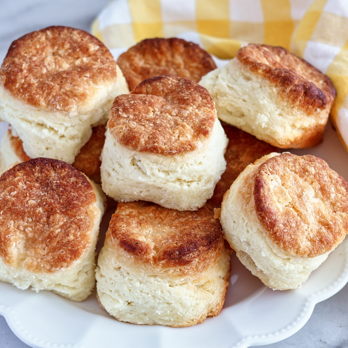 gluten free buttermilk biscuits stacked on white plate with yellow checked towel behind.