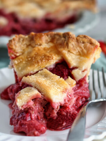 slice of gf strawberry rhubarb pie on stack of white plates with whole pie in the background.