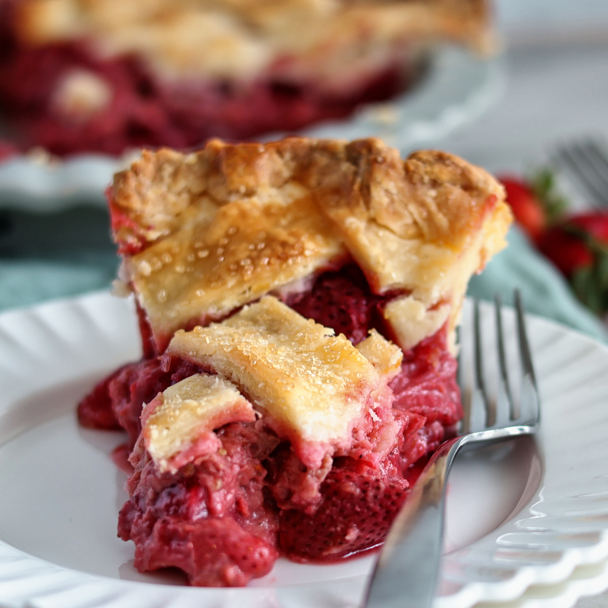 slice of gf strawberry rhubarb pie on stack of white plates with whole pie in the background.