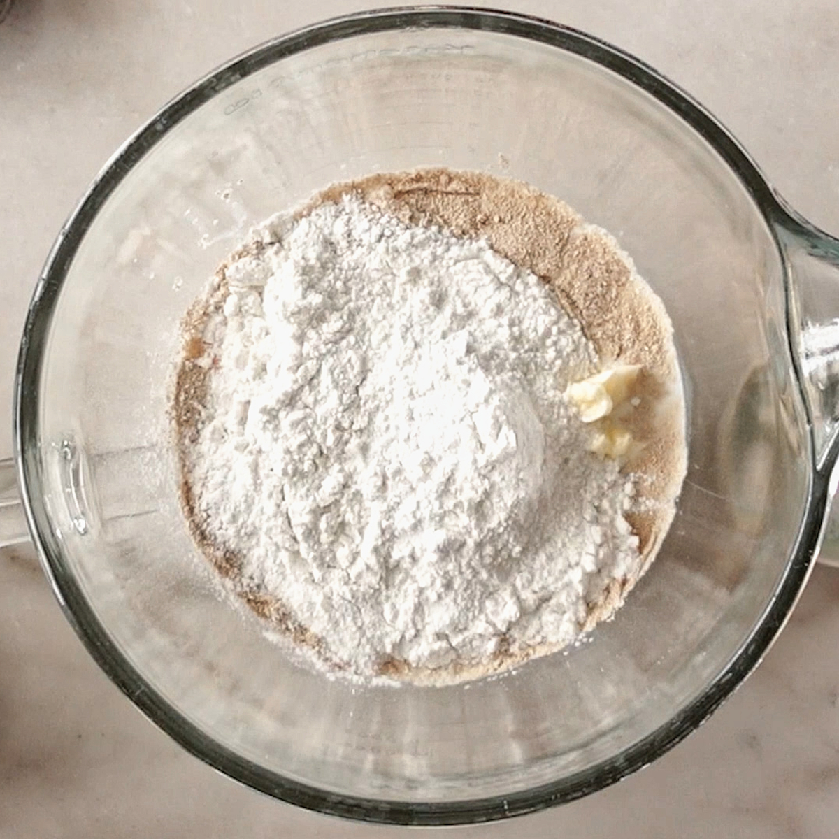 all ingredients for dough in glass stand mixer bowl.