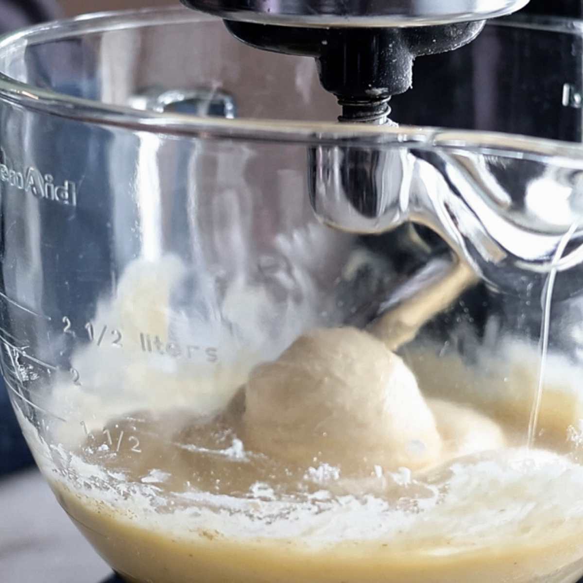 dough mixed in glass stand mixer bowl with dough hook.