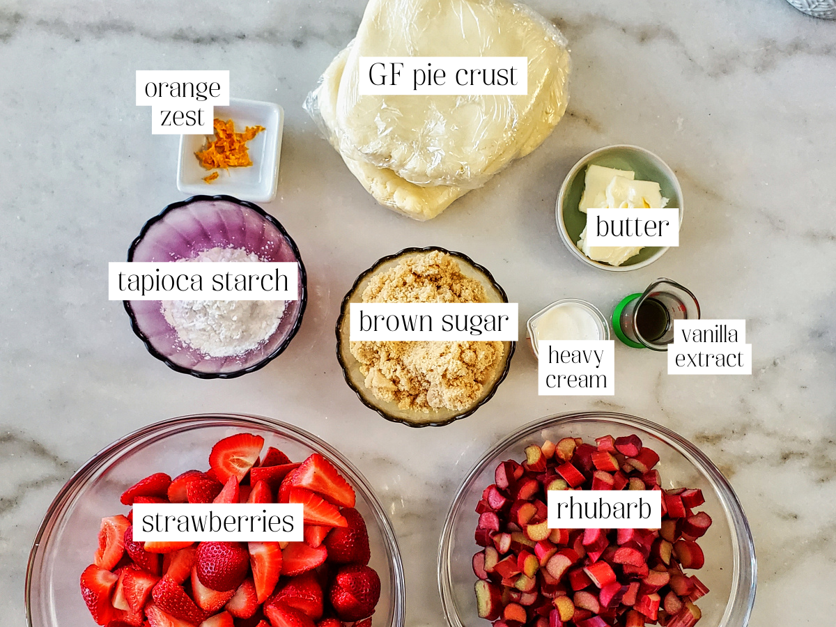 ingredients for strawberry rhubarb pie measured out and labeled on white marble counter.