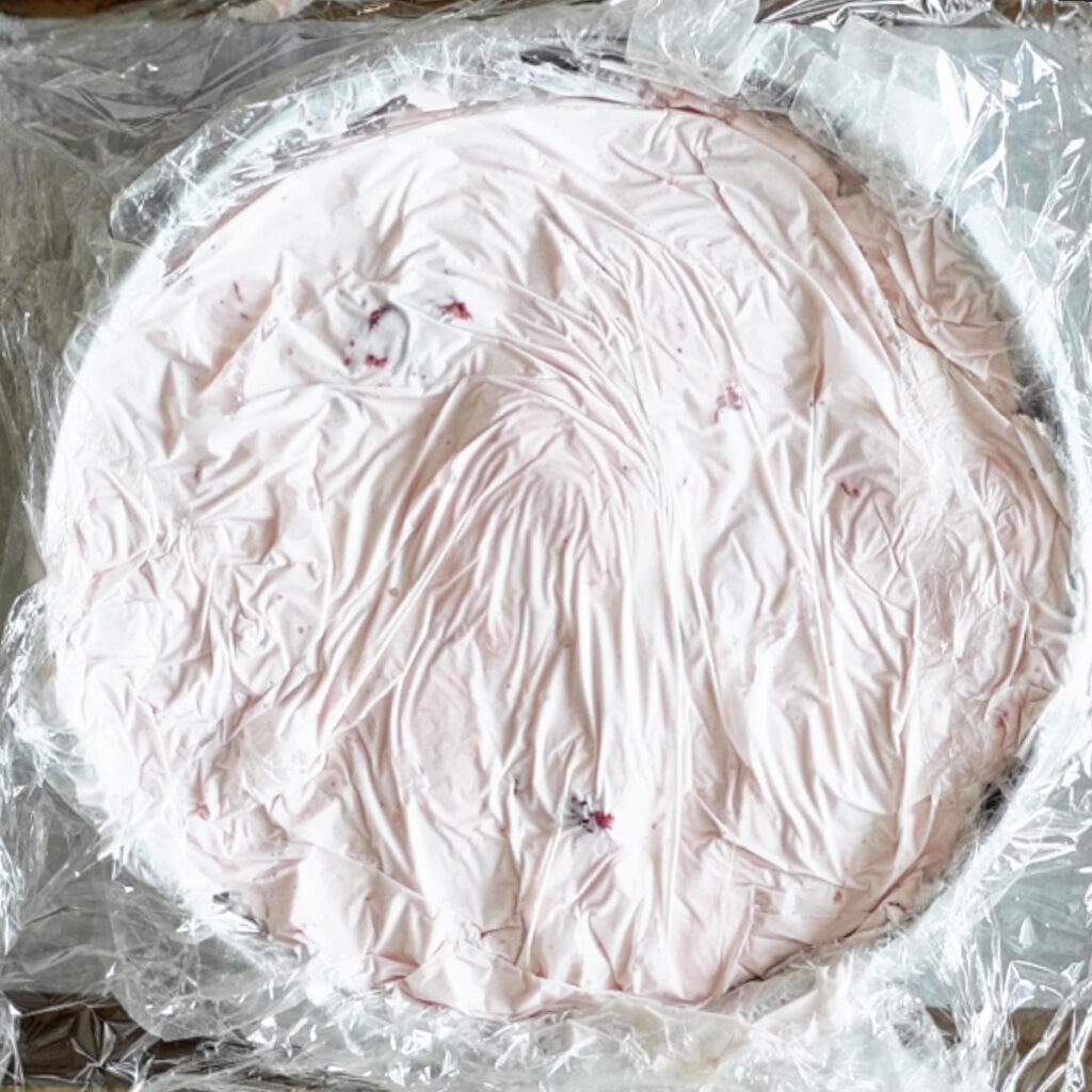 strawberry ice cream layered in cake ring with plastic wrap over it.