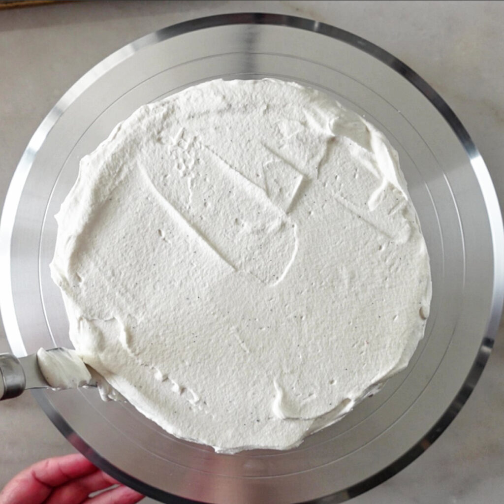 spreading whipped cream on sides of cake.