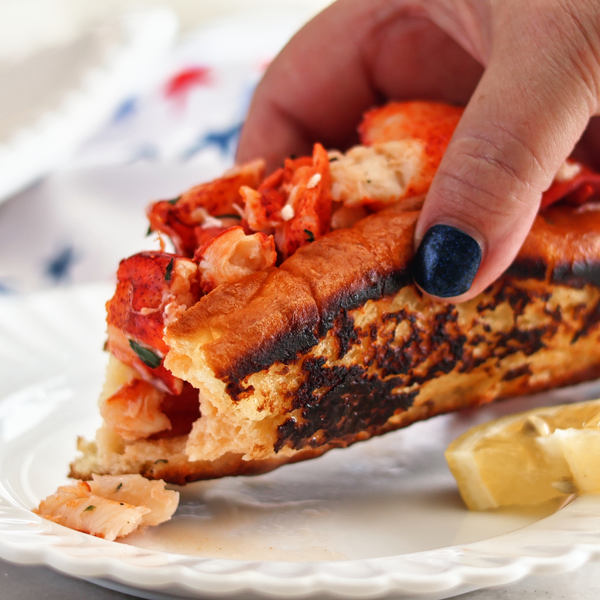 picking up lobster roll from white plate.