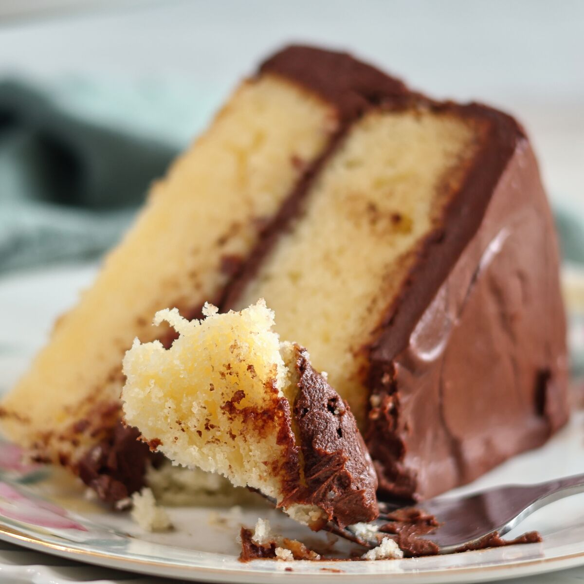 slice of yellow cake with chocolate frosting with bite on fork.
