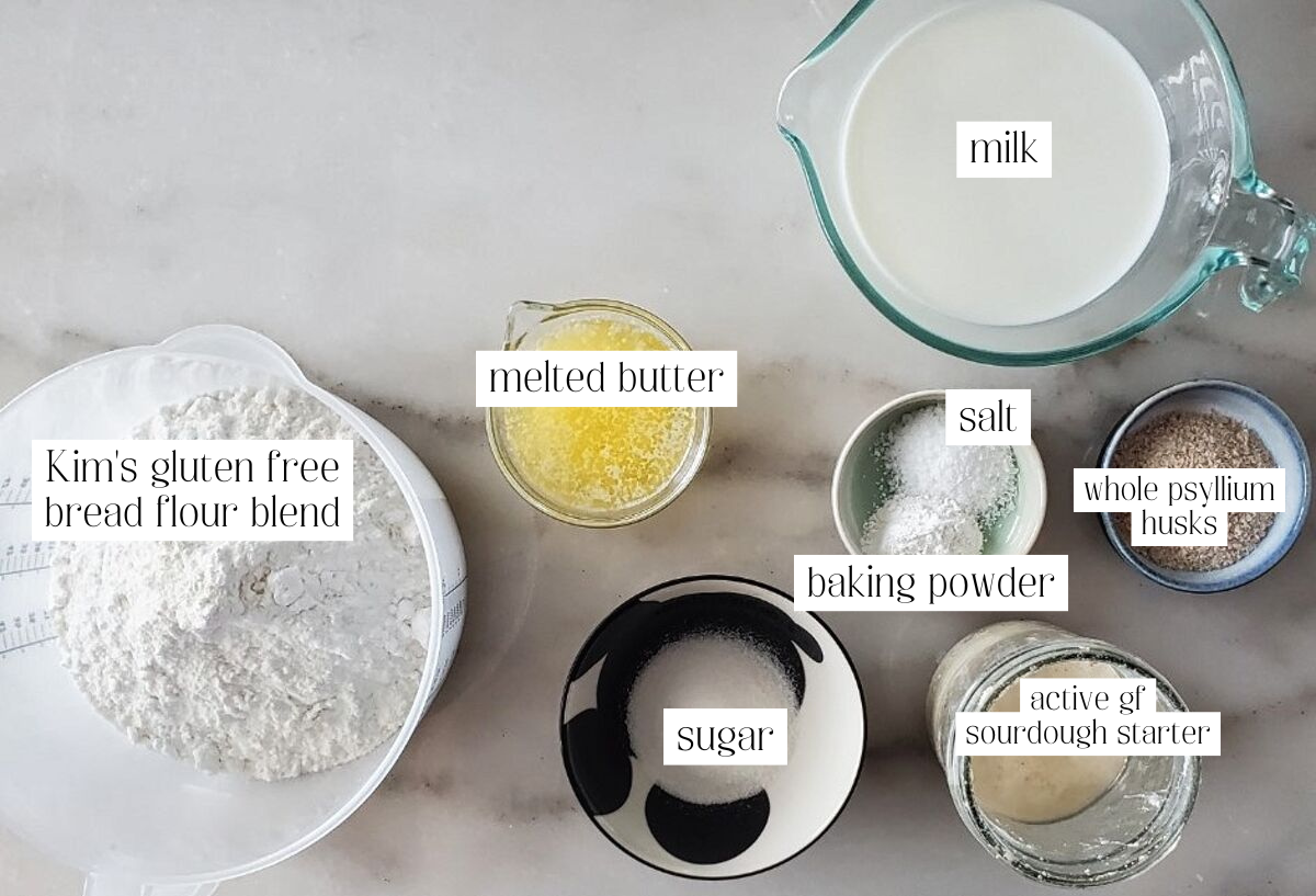 ingredients for sourdough sandwich bread measured out and labeled on white marble.