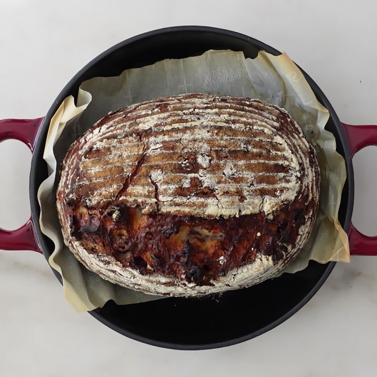 baked loaf of bread on parchment in red bread baker.