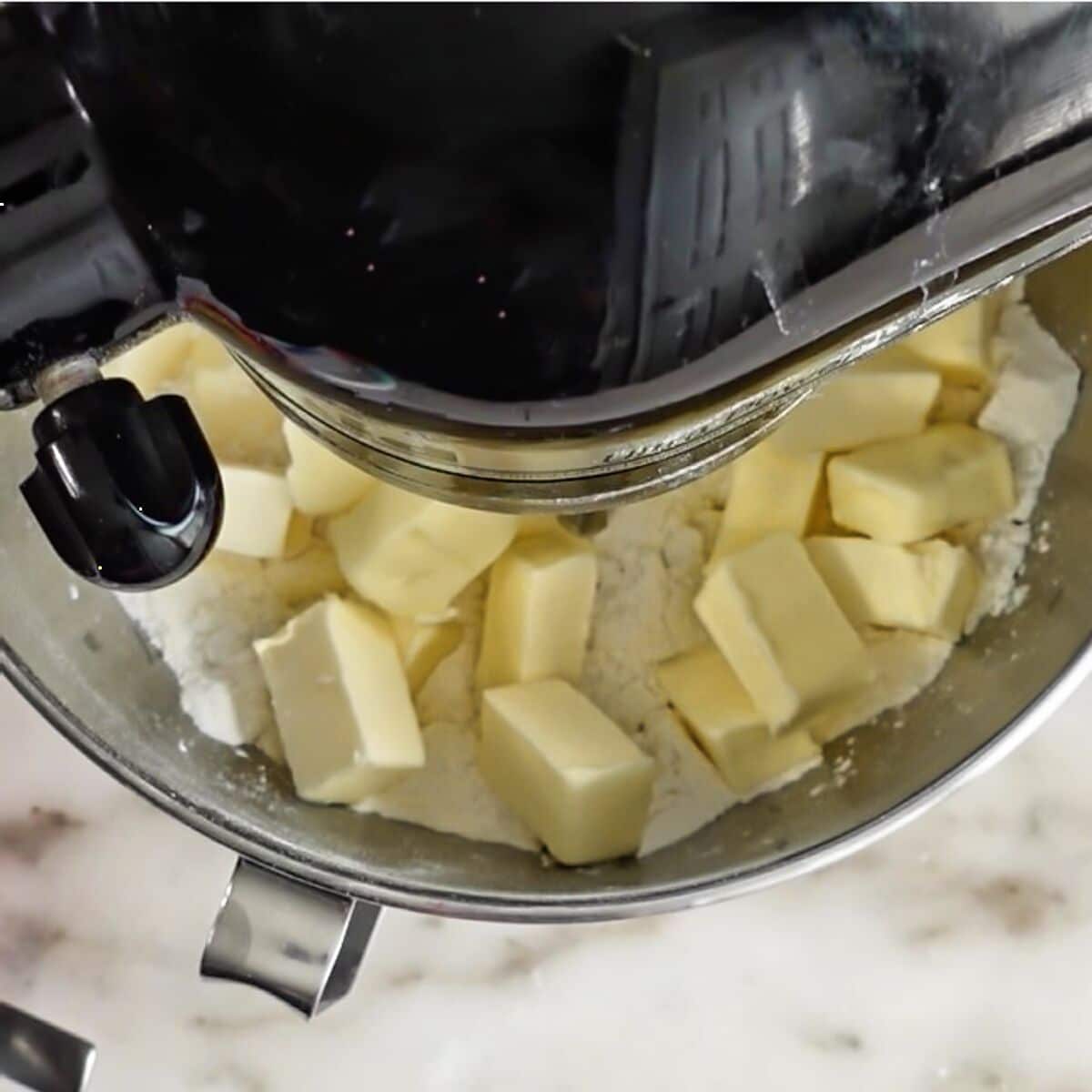 butter chunks on top of flour mixture in black stand mixer bowl.