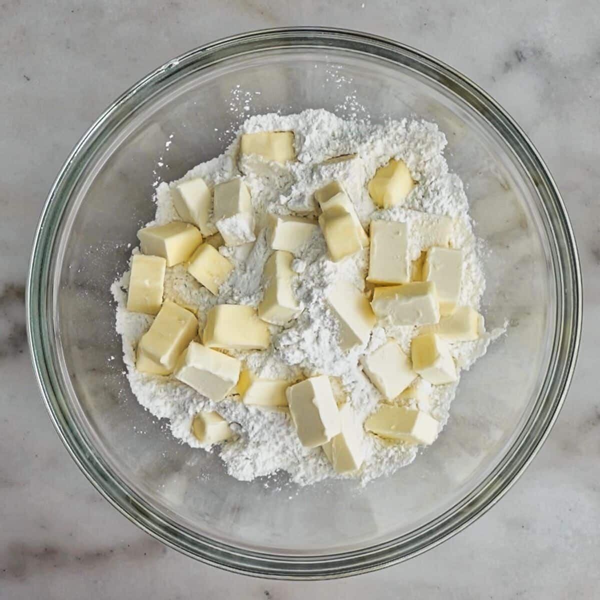 large chunks of butter on top of flour mixture in large glass bowl.