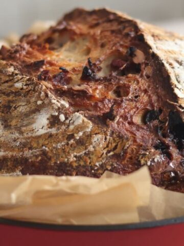 loaf of cranberry walnut bread in red bread baker with brown parchment around it.