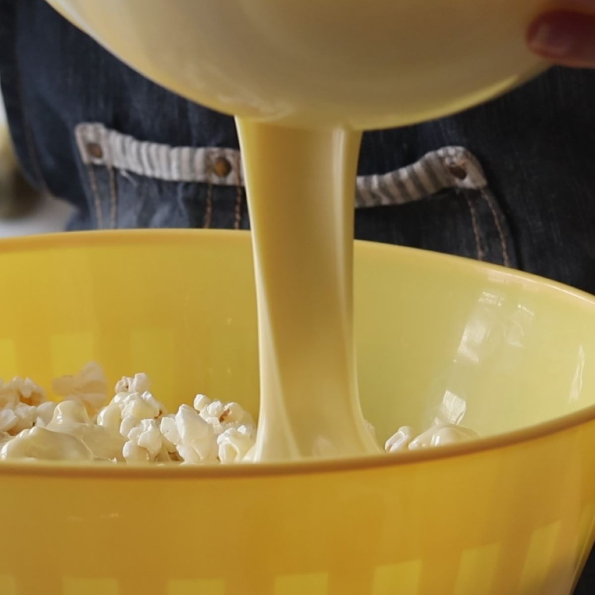 pouring white chocolate on top of popcorn in large yellow bowl.