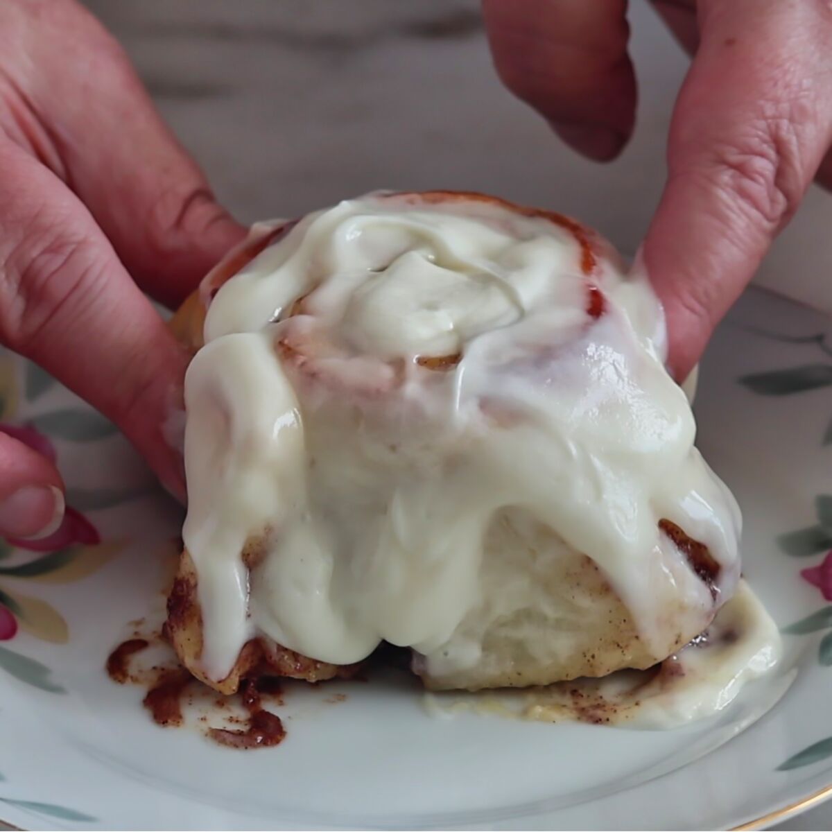 squishing cinnamon roll on plate with fingers.