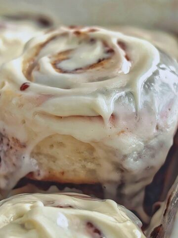 one large cinnamon roll on a metal spatula being lifted from baking dish.