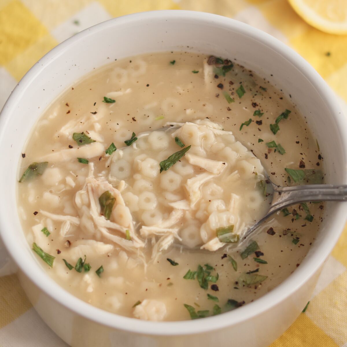 white bowl set on yellow checked napkin filled with chicken pastina soup and