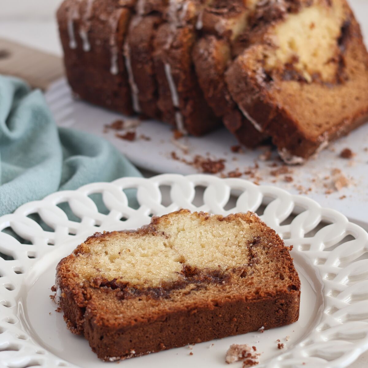 slice of cinnamon bread on white scalloped plate with whole loaf sliced in the background.