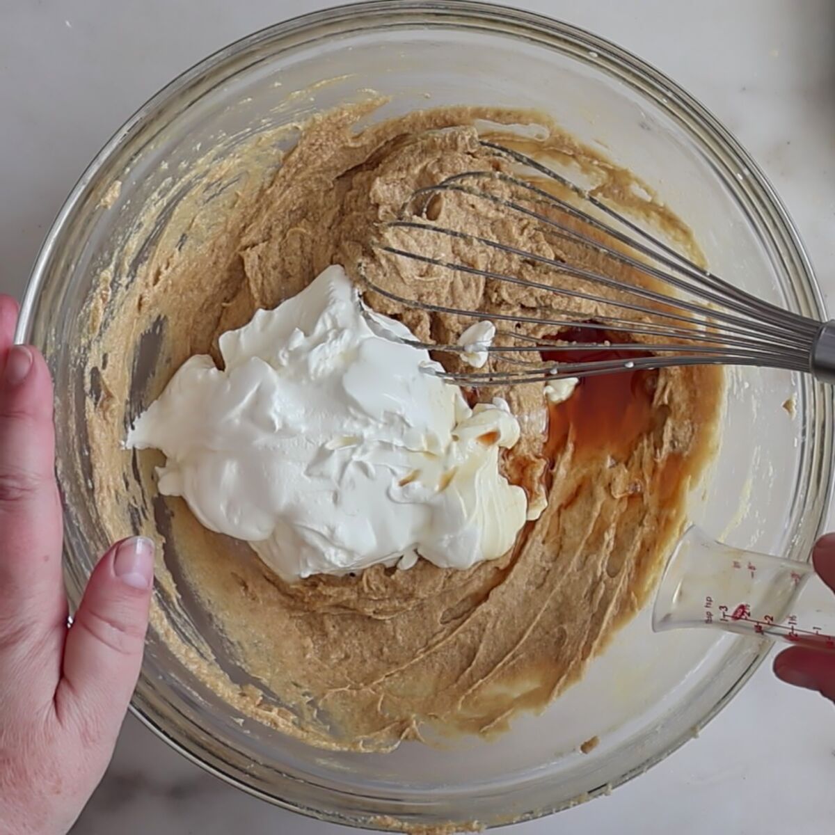 adding sour cream and vanilla to cake batter in glass bowl.
