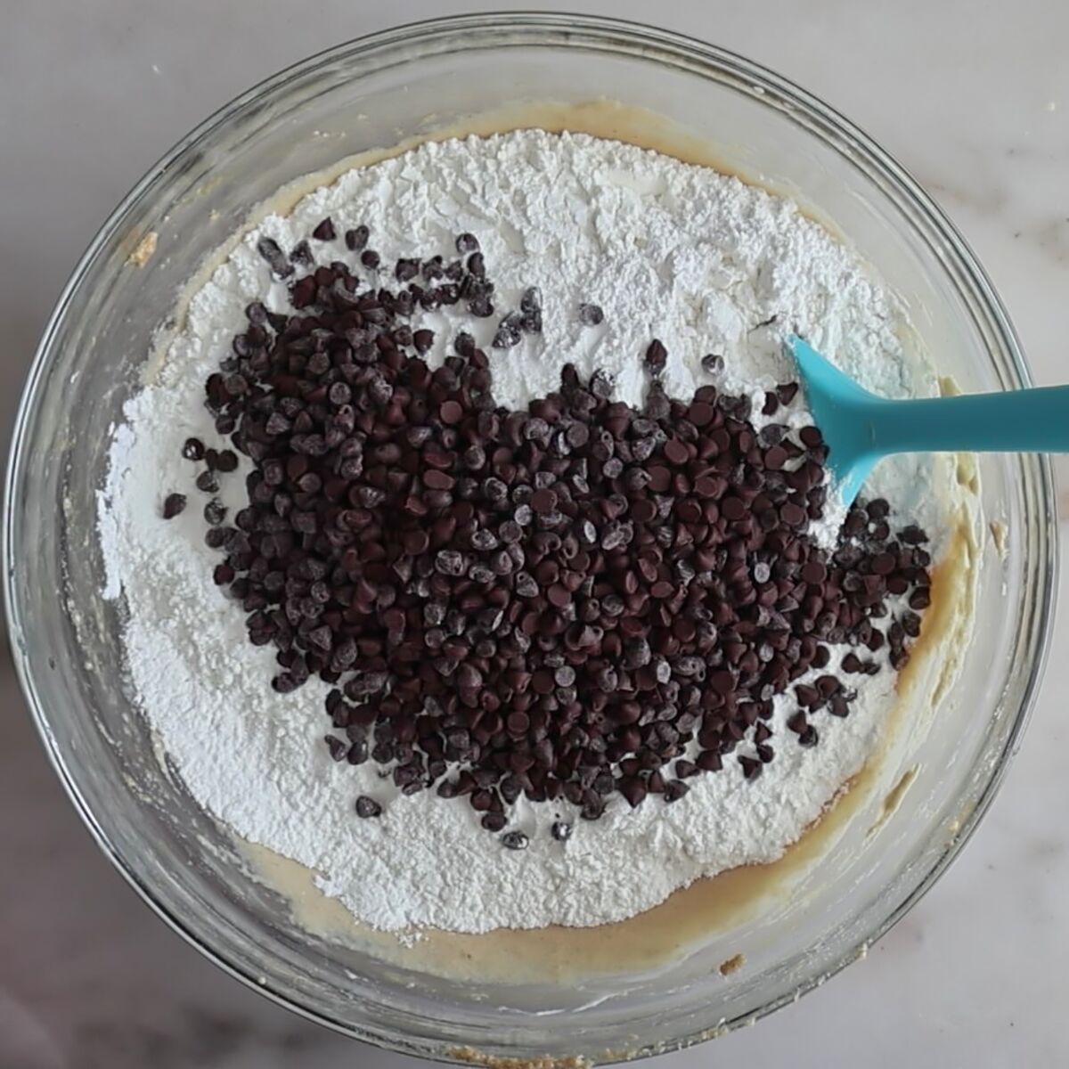 flour mixture and mini chocolate chips on top of batter in glass bowl.