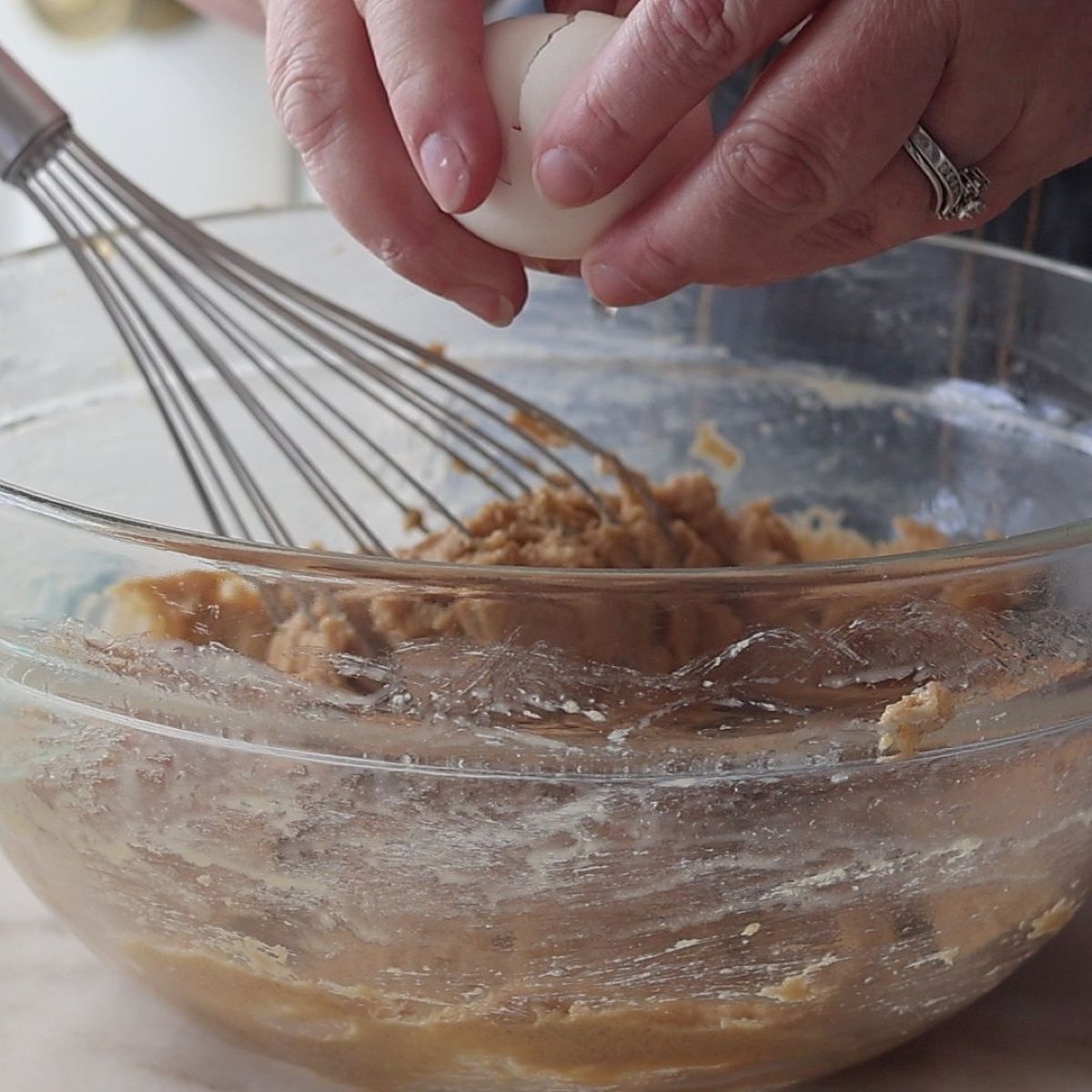 cracking egg over butter and sugar mixture in large glass bowl.