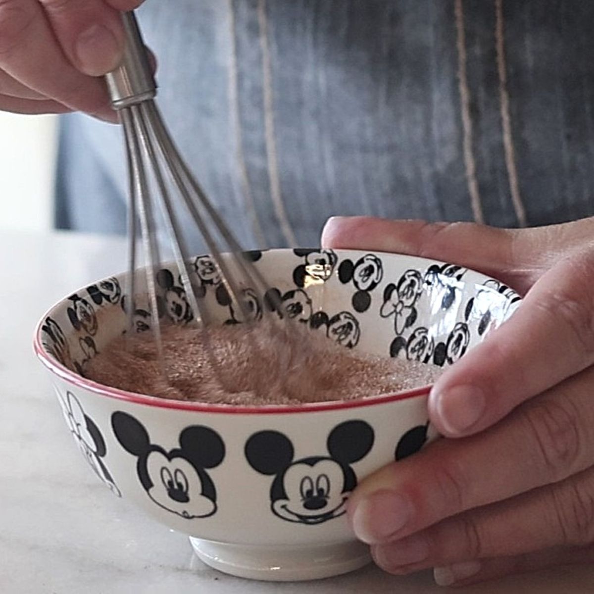 whisking together cinnamon and sugar in small mickey mouse bowl.