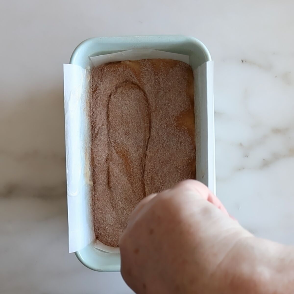 swirling cinnamon sugar topping in loaf pan with a butter knife.
