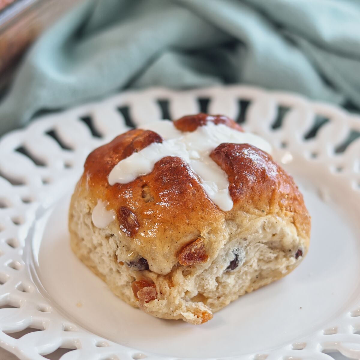 one hot cross bun on a scalloped white plate.