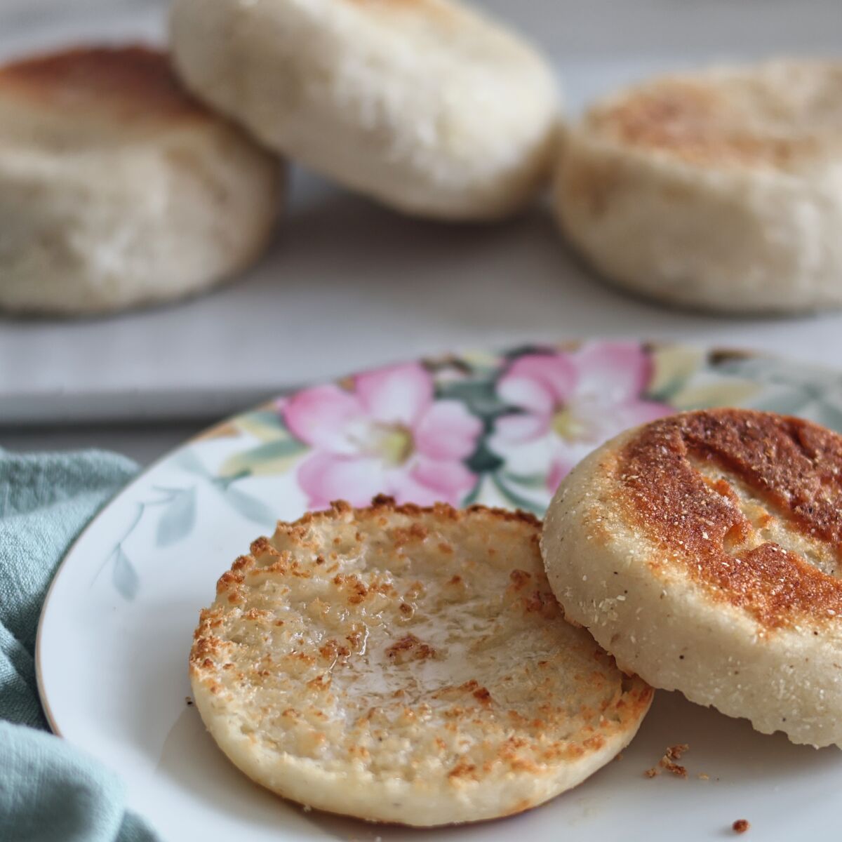 split english muffin on flowered plate with whole english muffins in the background.