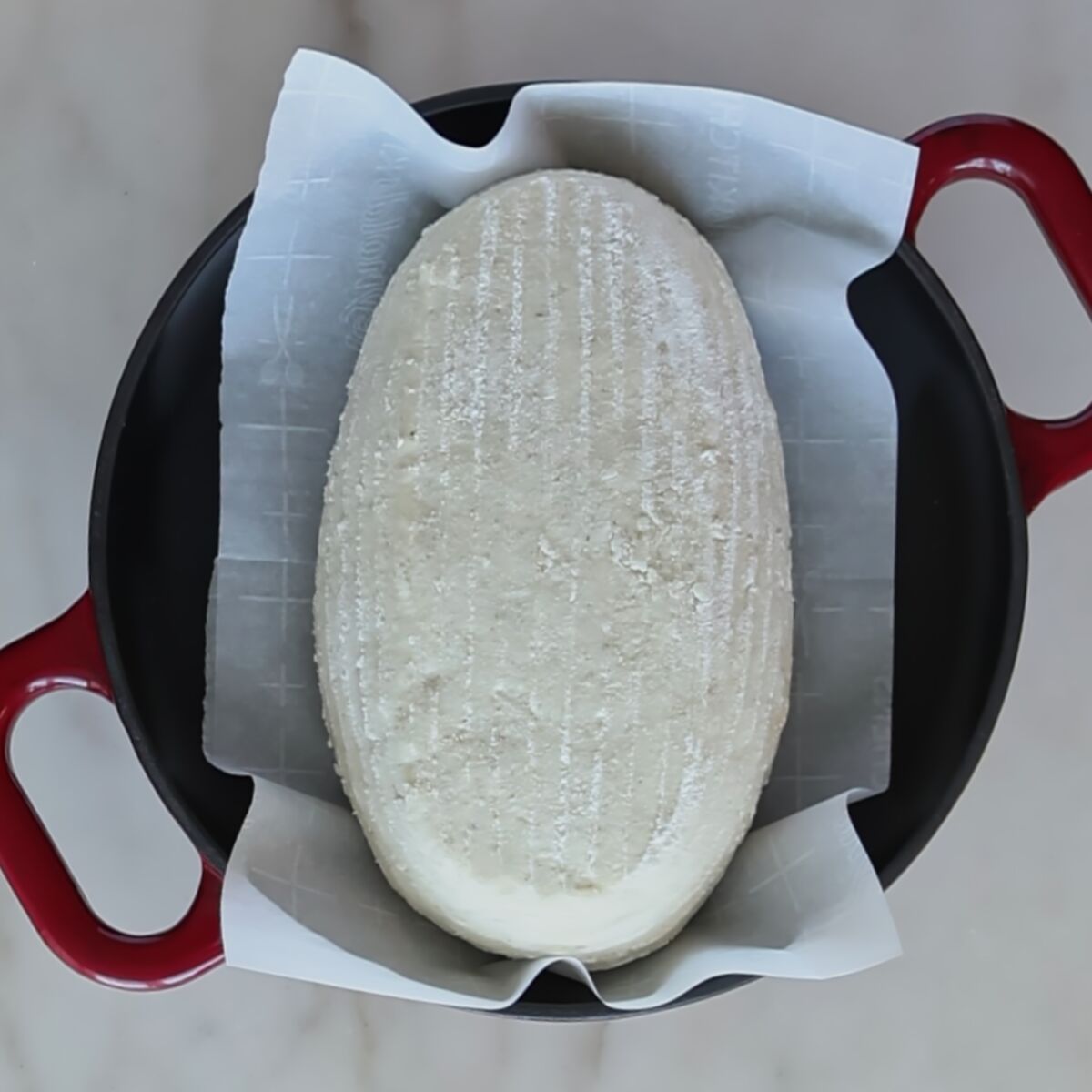 shaped sourdough loaf on parchment inside red dutch oven.
