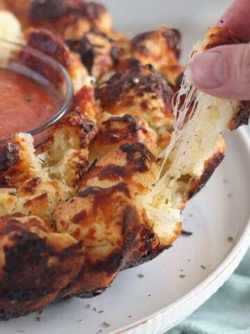 pulling off a piece of pull apart pizza biscuits with a long cheese pull.