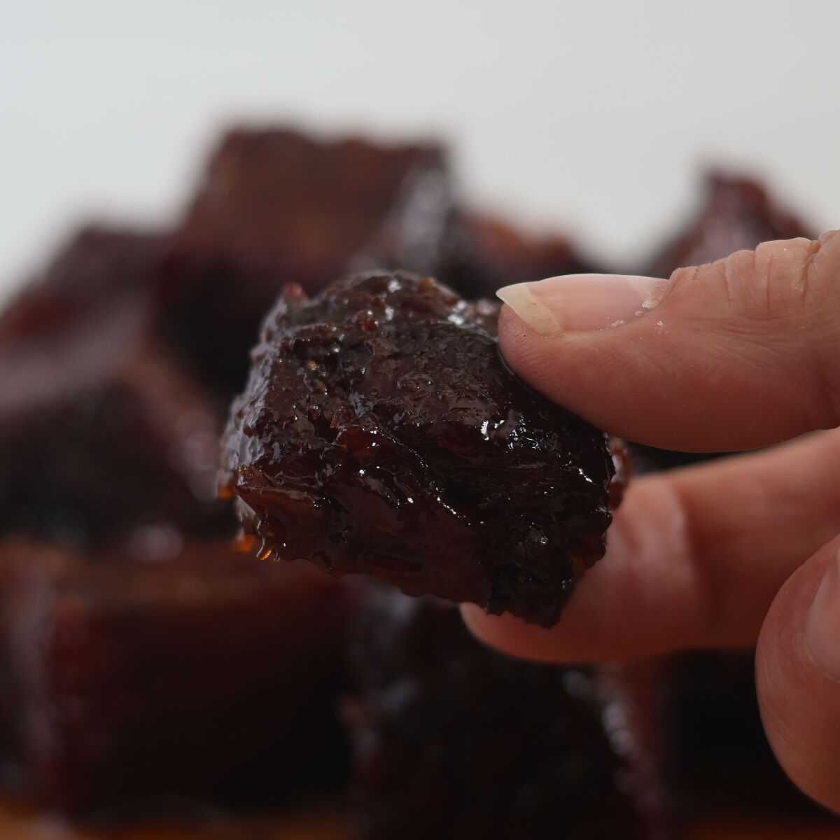 holding a cube of burnt ends in fingers.