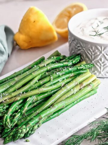 asparagus on white rectangular platter with dip alongside.