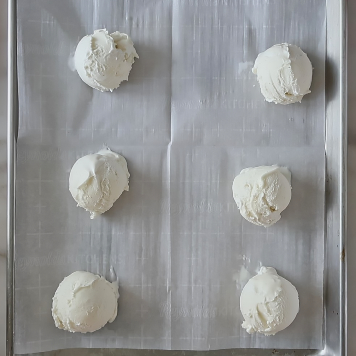 vanilla ice cream balls on parchment-lined baking sheet.