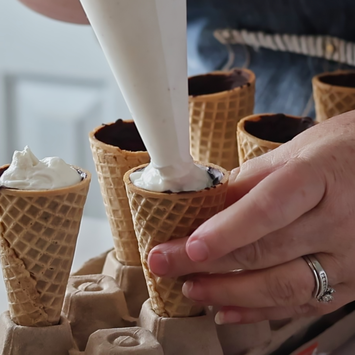 piping vanilla ice cream into chocolate lined ice cream cones.