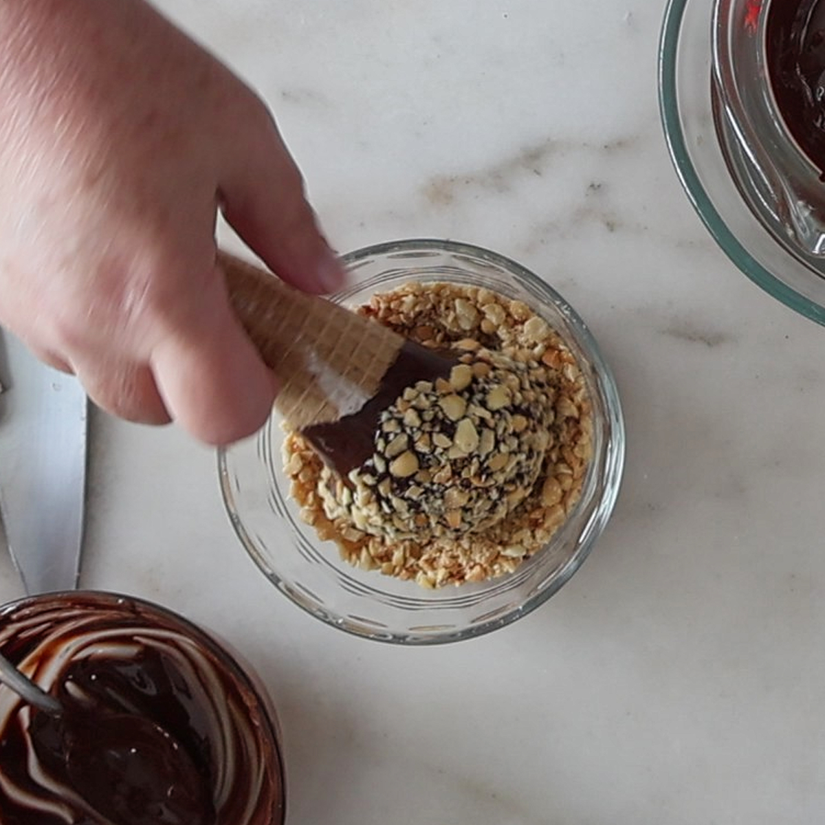 rolling chocolate dipped ice cream cone in chopped nuts.