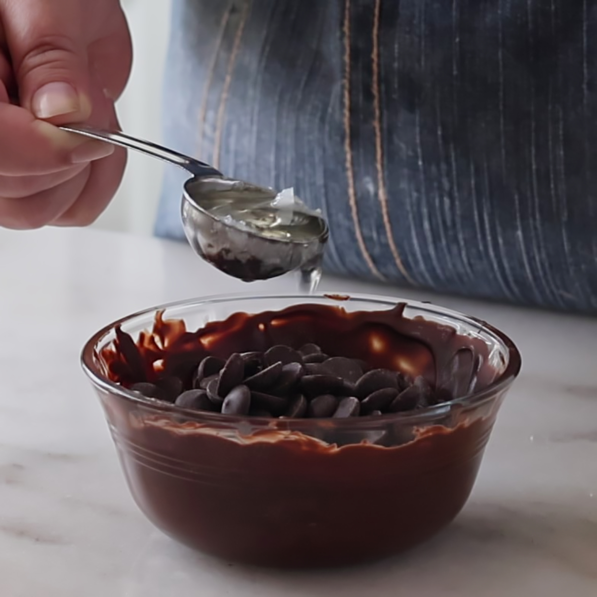 adding coconut oil to chocolate chips in small glass bowl.