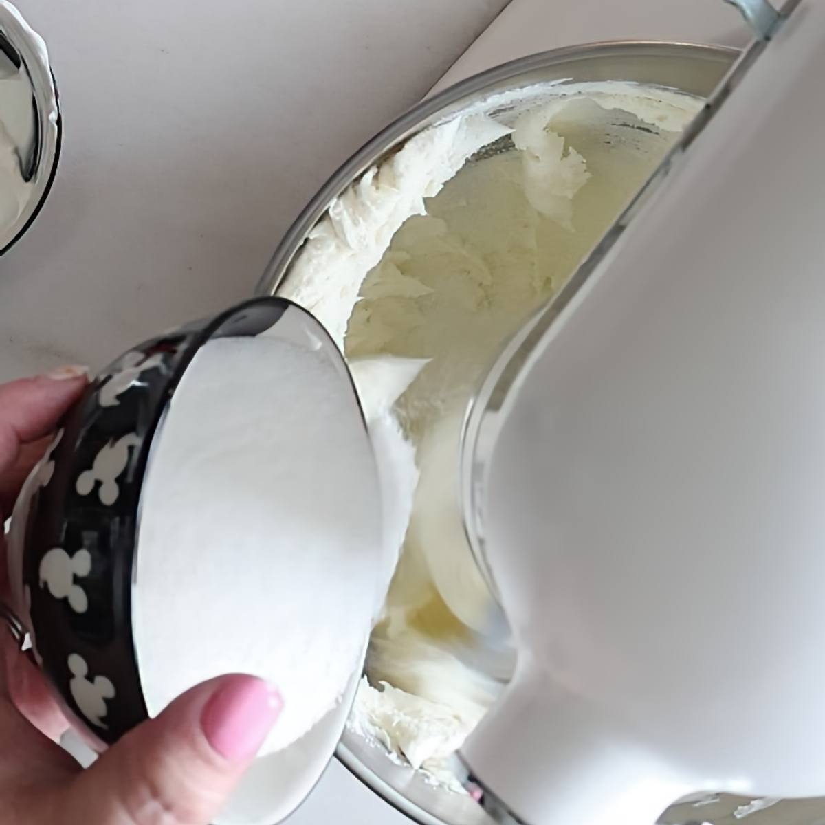 adding sugar to cream cheese in white stand mixer.