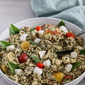 white bowl of orzo pesto salad with green towel in the background.