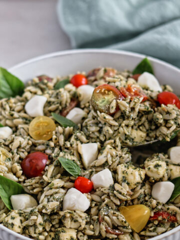 white bowl of orzo pesto salad with green towel in the background.