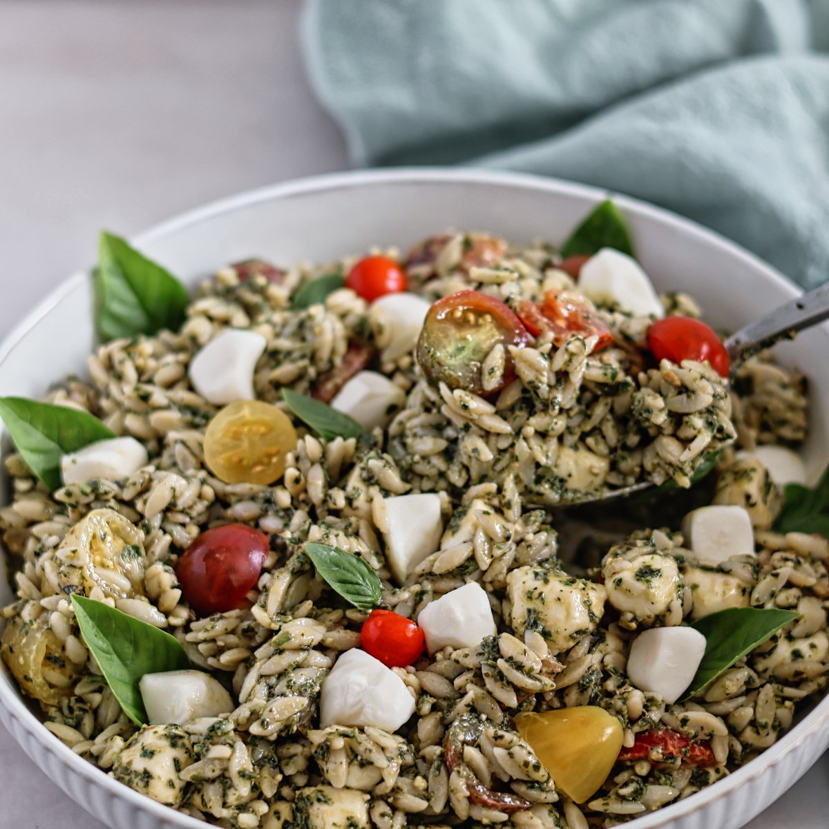 white bowl of orzo pesto salad with green towel in the background.