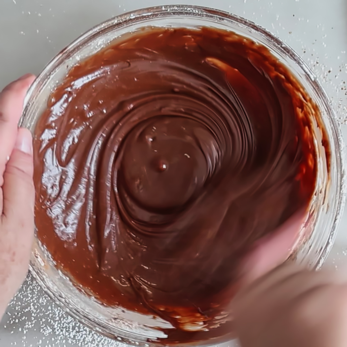 stirring shiny chocolate glaze in glass bowl.