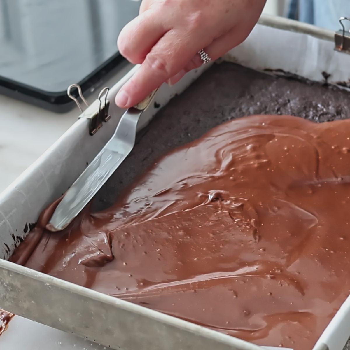 spreading shiny chocolate glaze on brownies in rectangular pan.